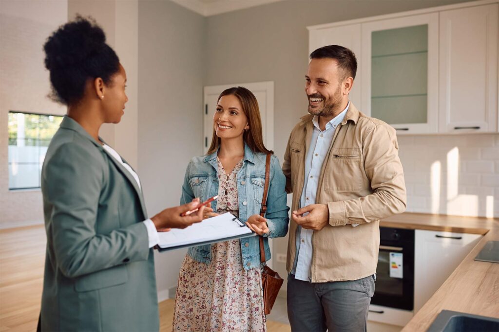 Happy couple discussing home purchase details with a real estate agent in a modern kitchen, symbolizing the home-buying process.